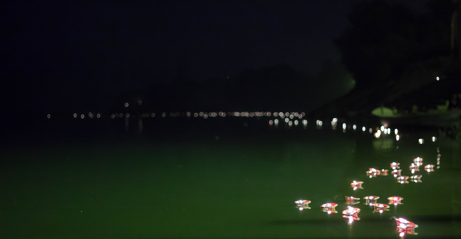 Diya lamps floating on the Ganges at night with bokeh lights of Ram Jhula bridge in the background, Rishikesh