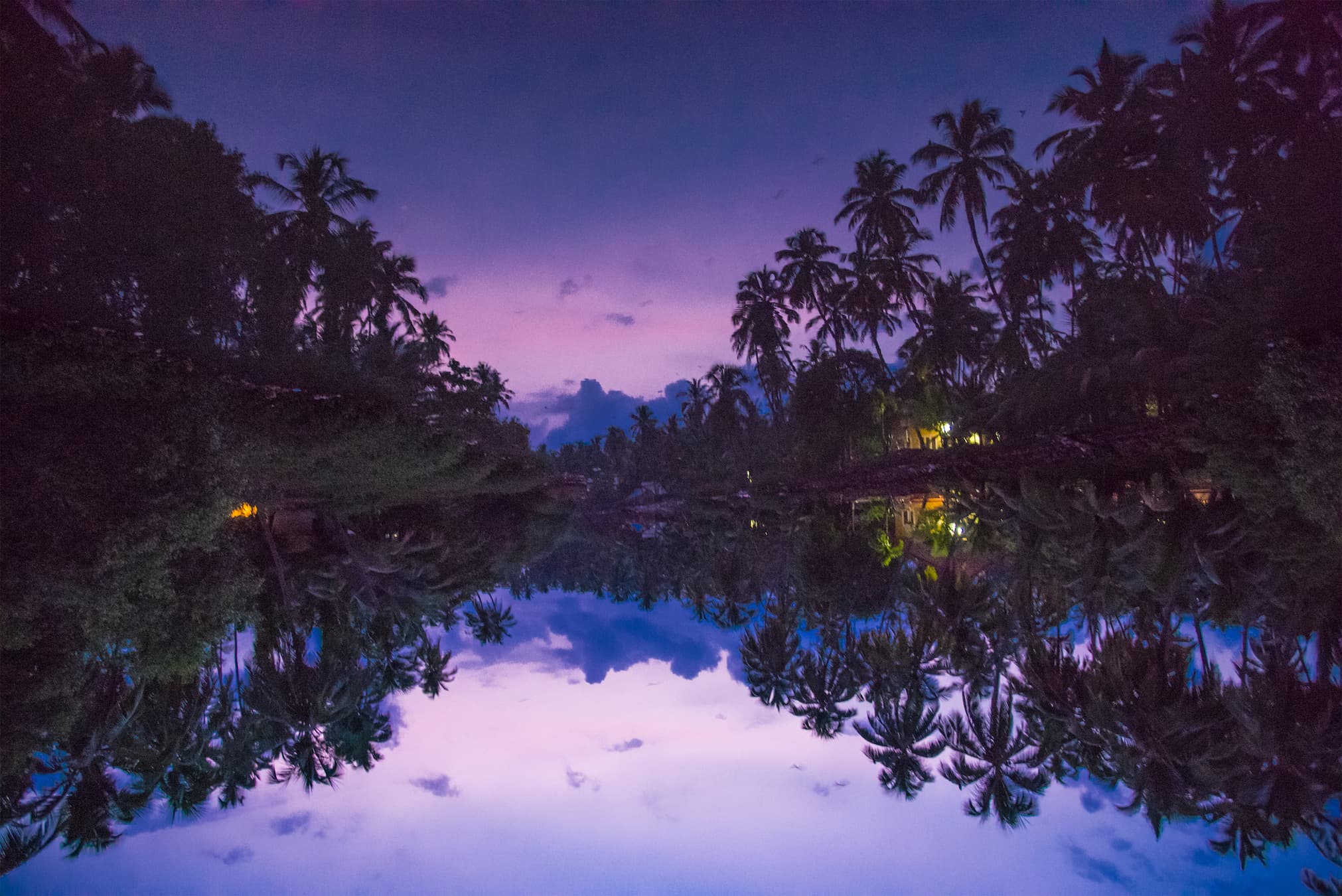 Kerala backwaters at dusk, a traditional wooden houseboat gliding through palm-lined waterways reflecting golden evening light