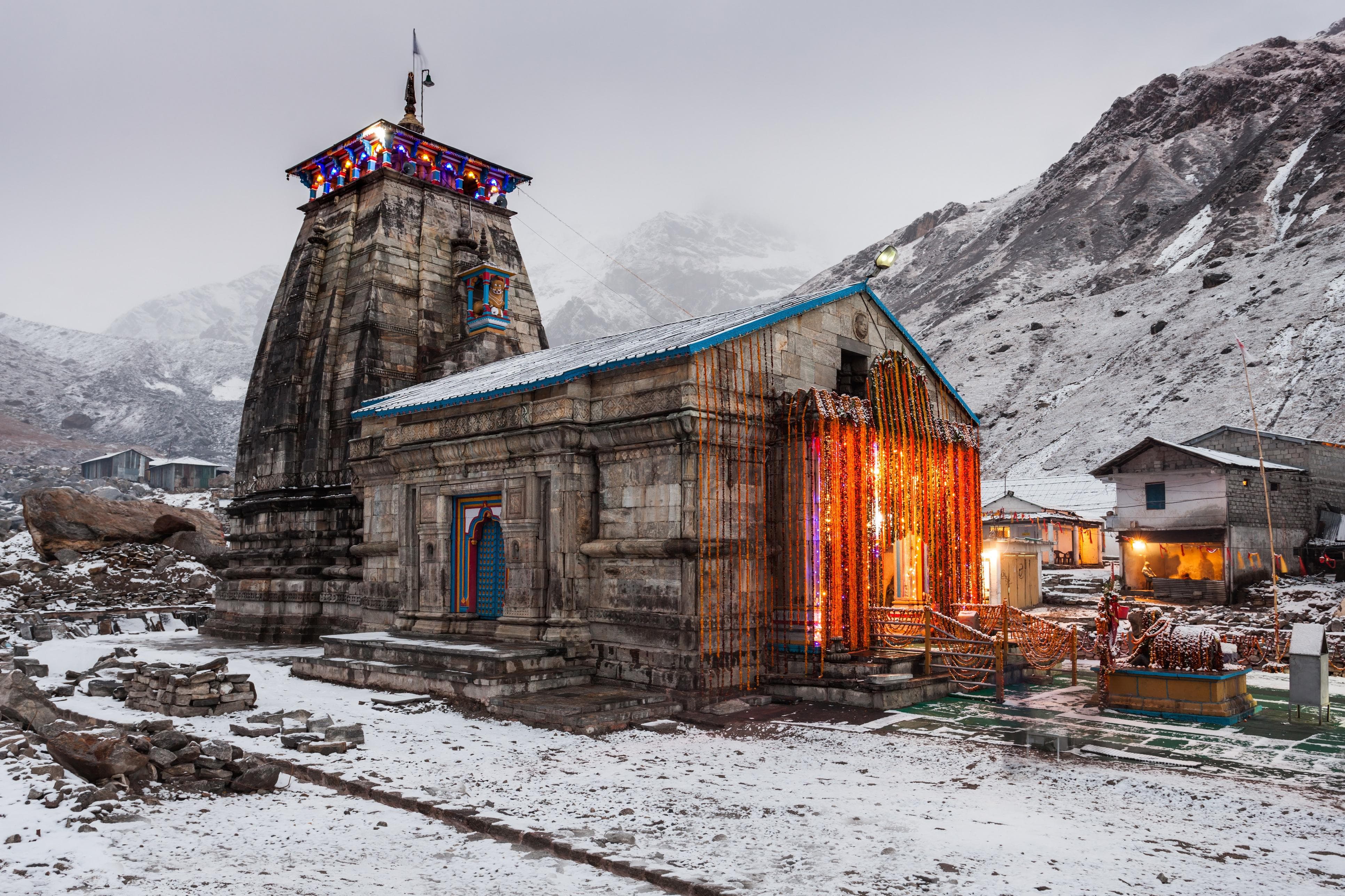 Kedarnath temple covered in snow with marigold garland decorations glowing against the glacial Himalayan peaks at dusk