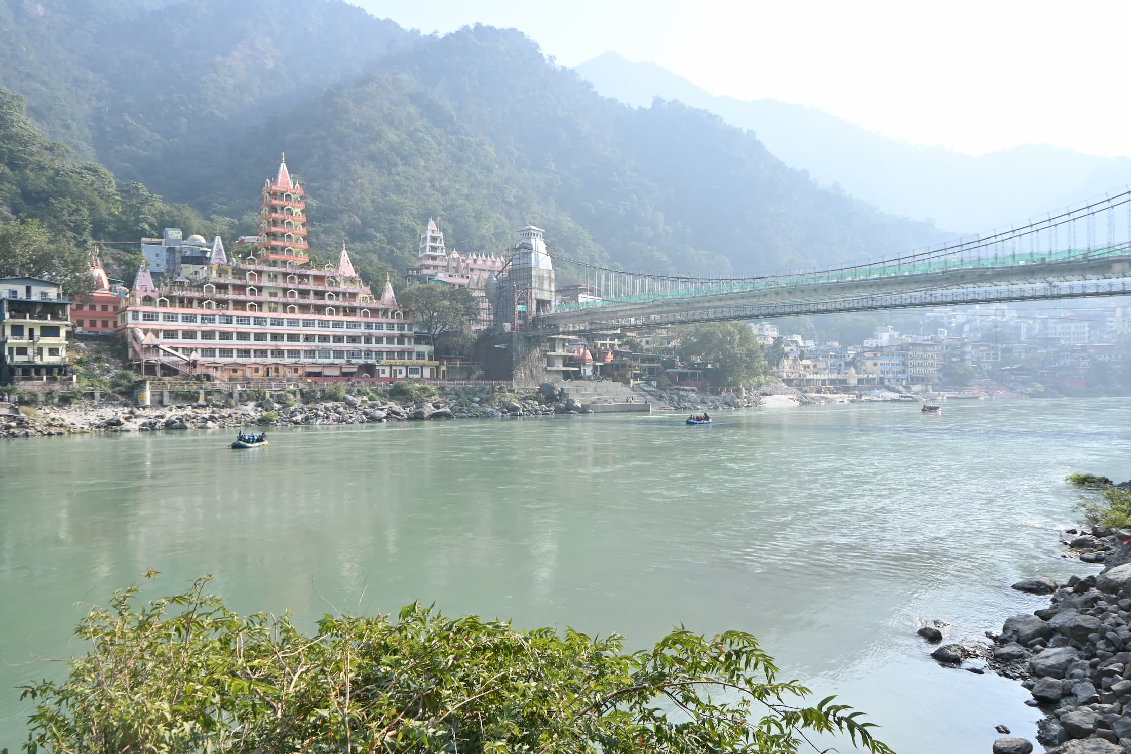 Laxman Jhula suspension bridge spanning the Ganga with temples and forested hills in the mist at Rishikesh